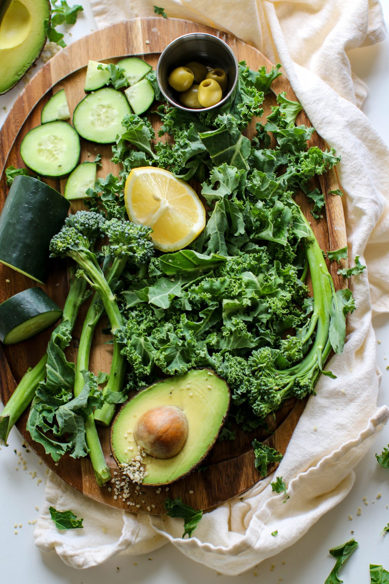 wooden board topped with cucumber, avocado, broccoli, and olives by Flora & Vino
