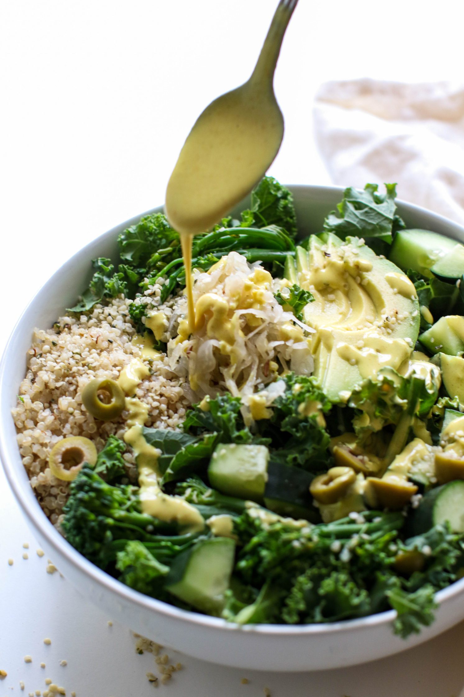 Green Macro Bowl with Turmeric Tahini drizzled off spoon by Flora & Vino