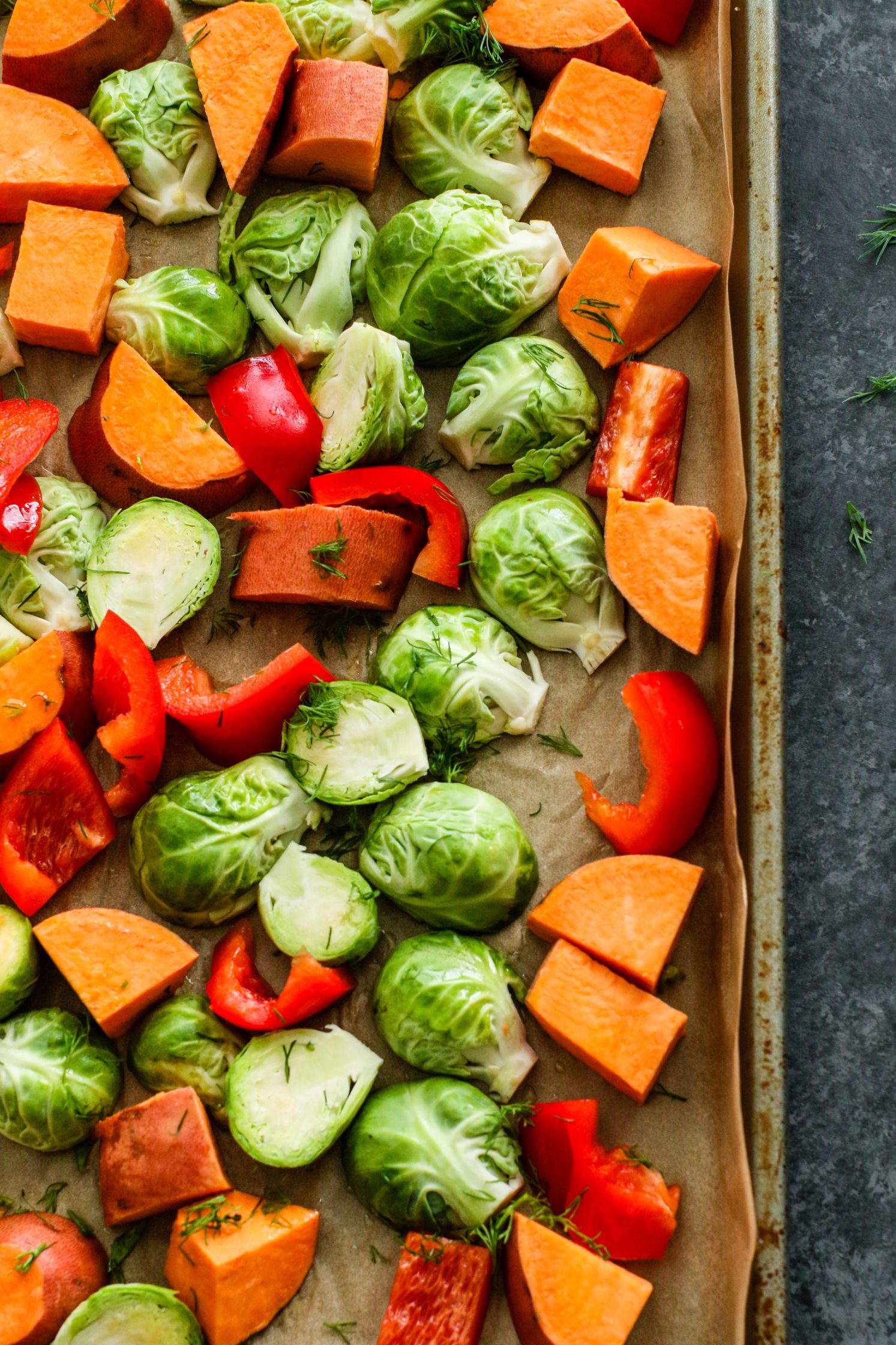 sweet potato, brussels sprouts, and red pepper with dill on parchment lined baking sheet by Flora & Vino