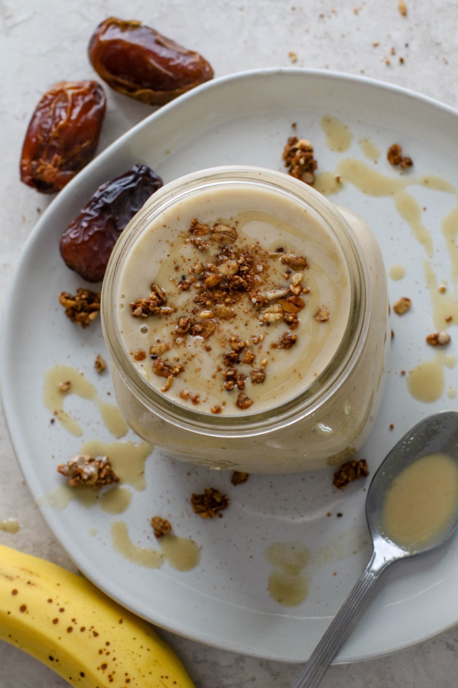 Tahini Date Shake served in a mason jar on a plate topped with granola and tahini with dates and banana on the side by Flora & Vino