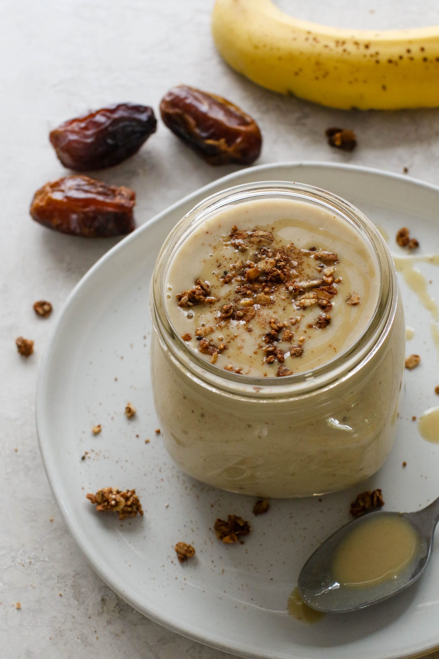 Tahini Date Shake served in a mason jar on a plate topped with granola and tahini with dates and banana on the side by Flora & Vino
