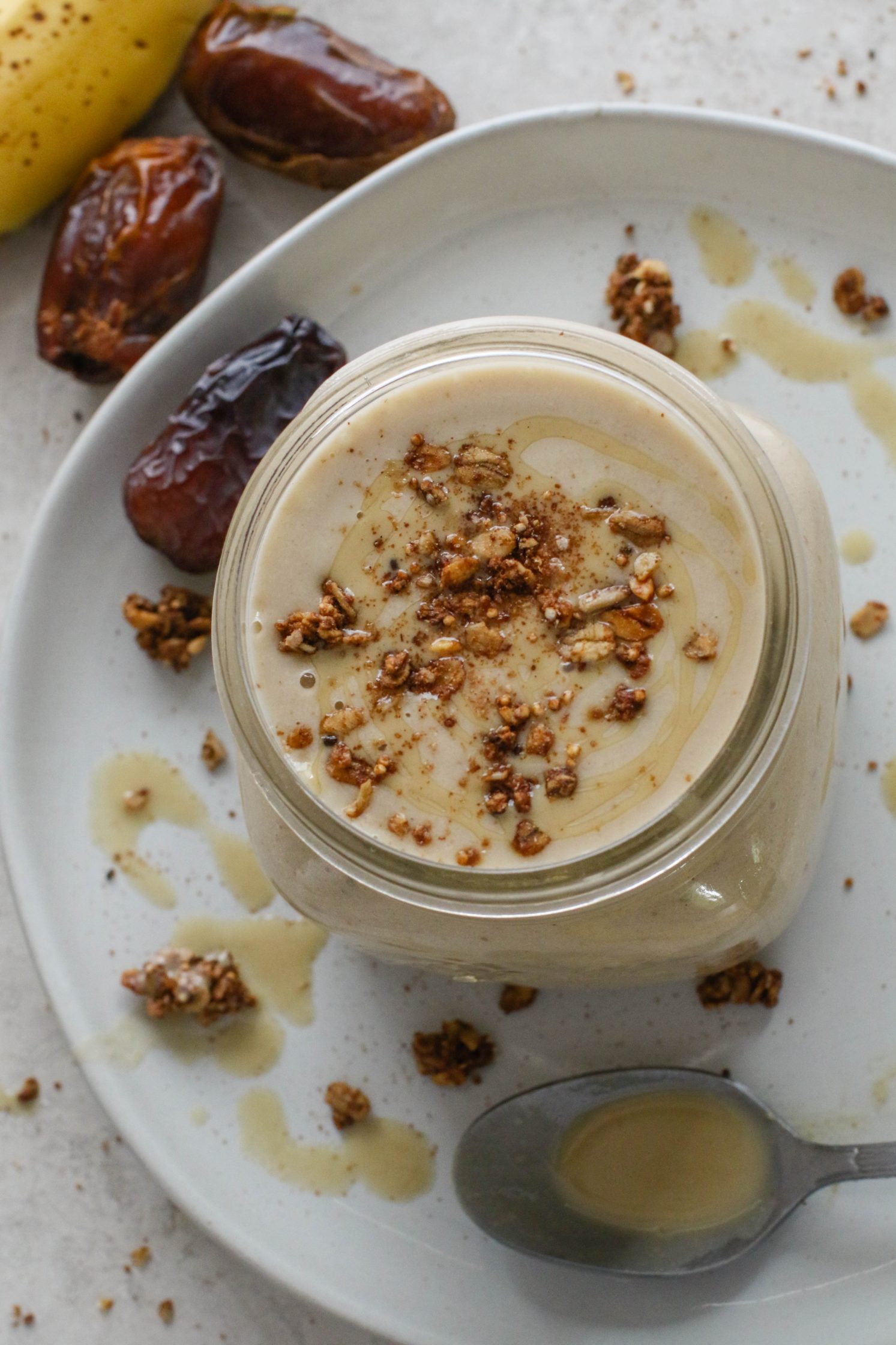 Tahini Date Shake served in a mason jar on a plate topped with granola and tahini with dates and banana on the side by Flora & Vino