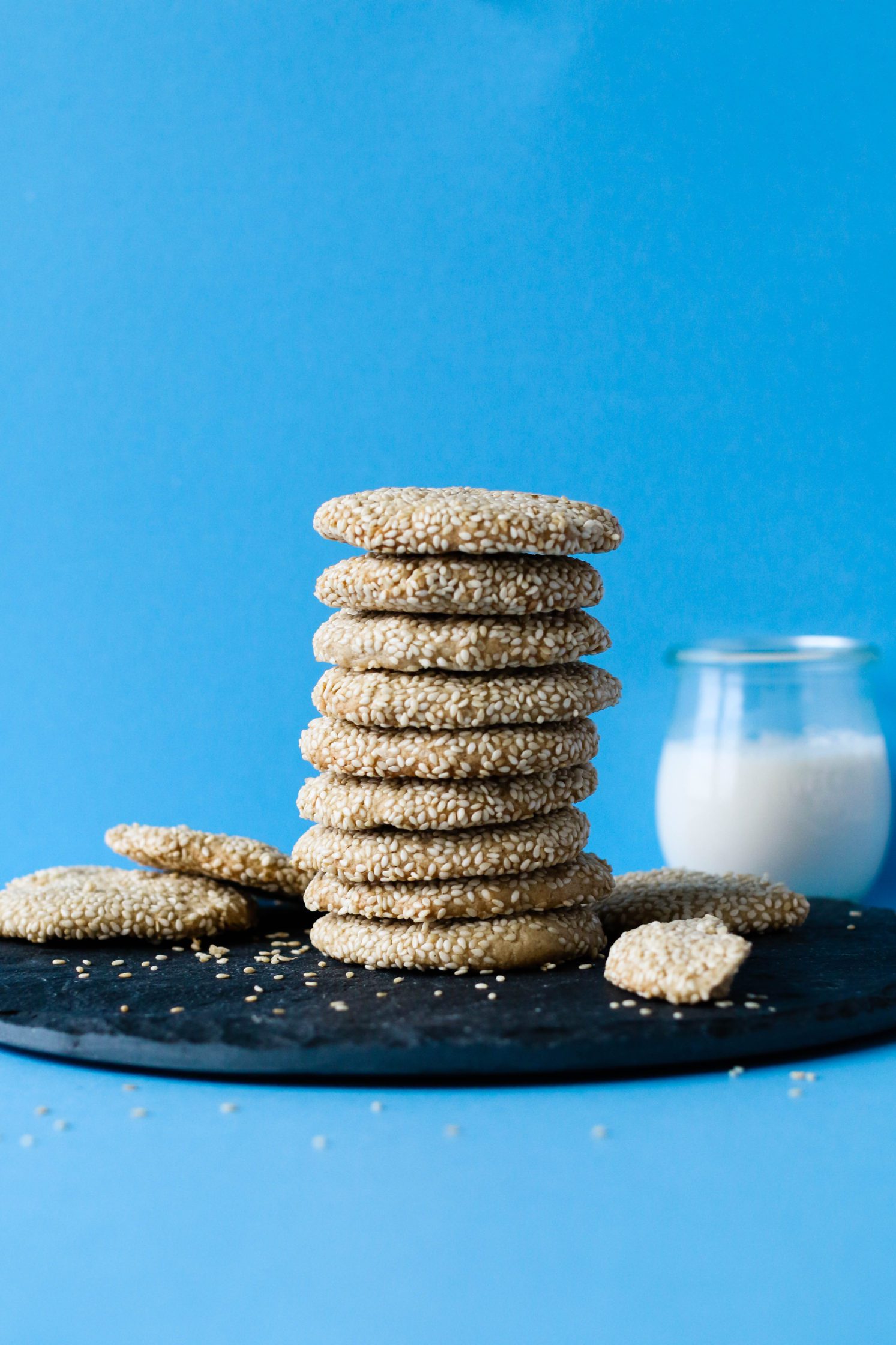 4 Ingredient Maple Sesame Tahini Cookies stacked on board with milk behind them by Flora & Vino