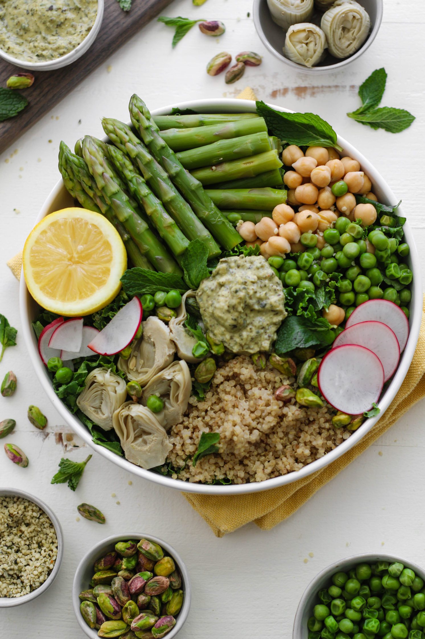 Spring Macro Bowl in large bowl with asparagus, lemon, artichoke hearts, sliced radishes, chickpeas, peas, quinoa, and mint