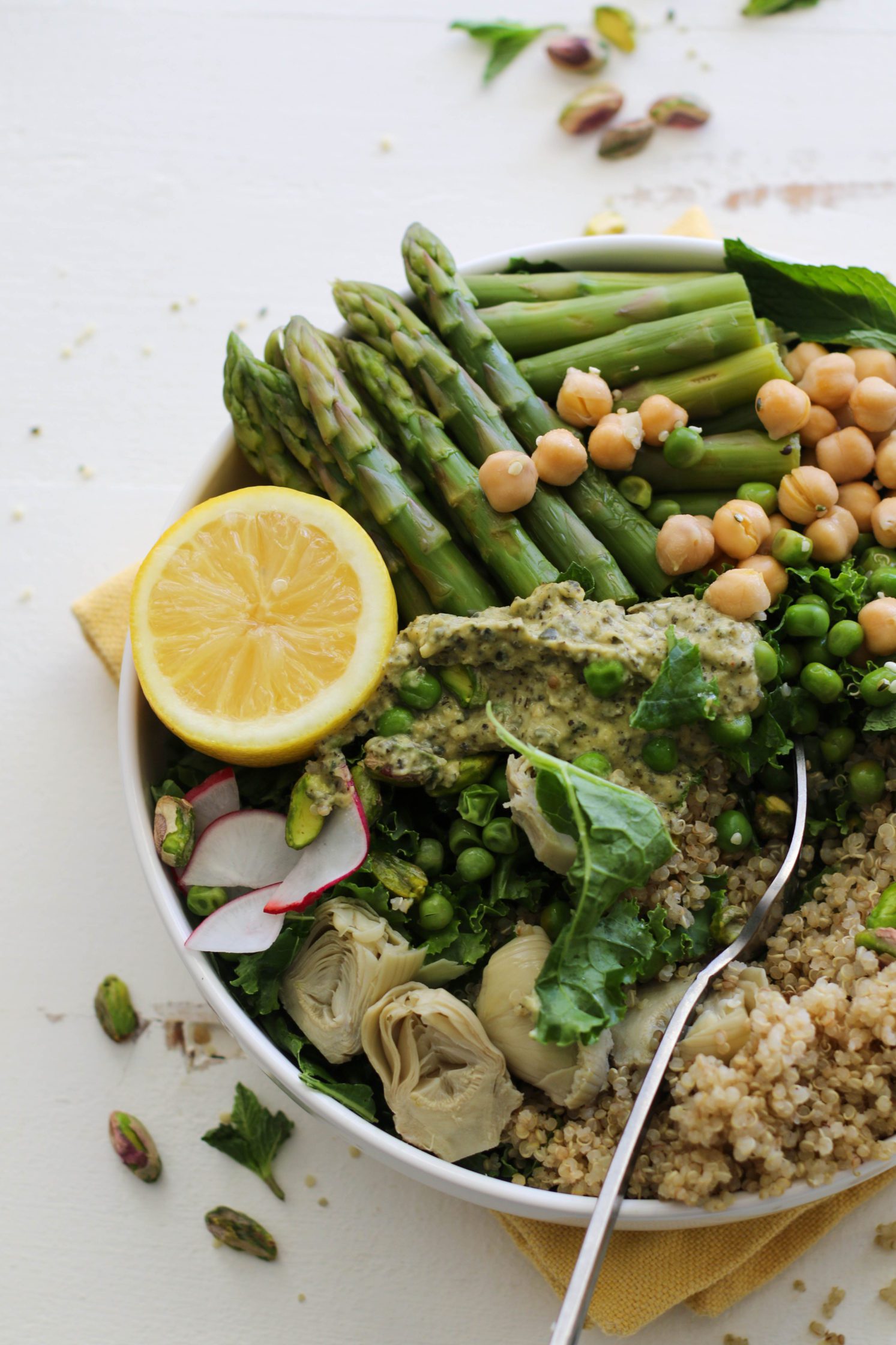 Spring Macro Bowl in large bowl with asparagus, lemon, artichoke hearts, sliced radishes, chickpeas, peas, quinoa, and mint
