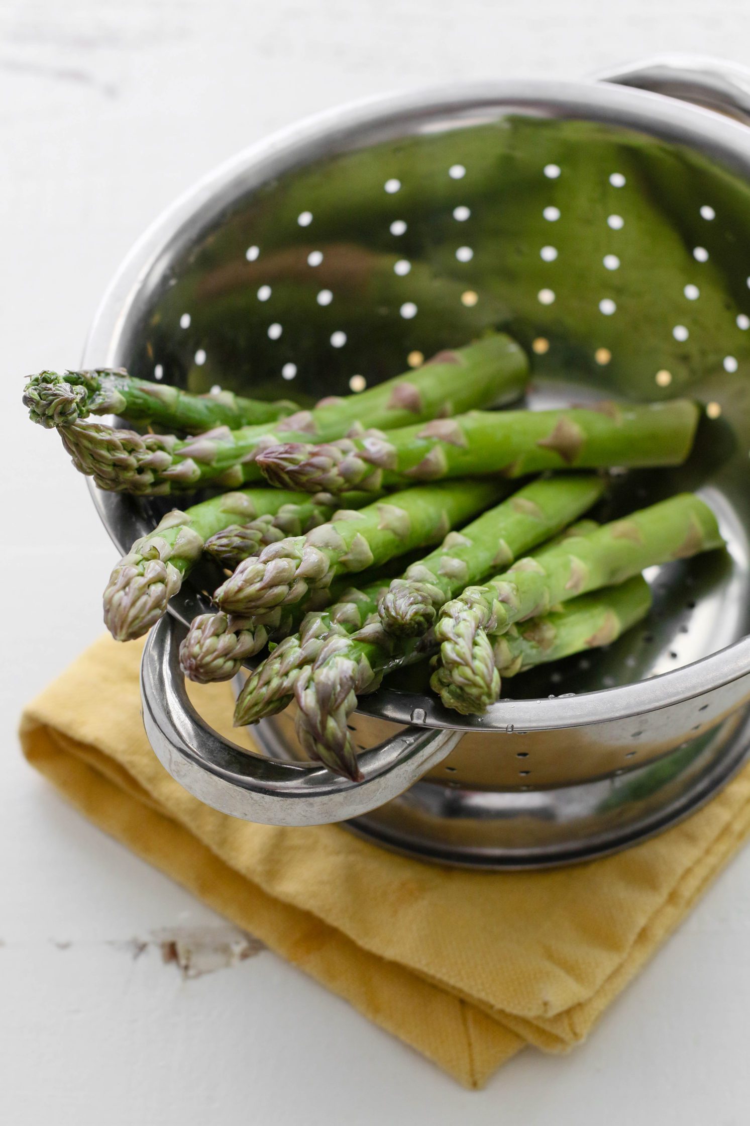 raw asparagus in colander with yellow towel underneath