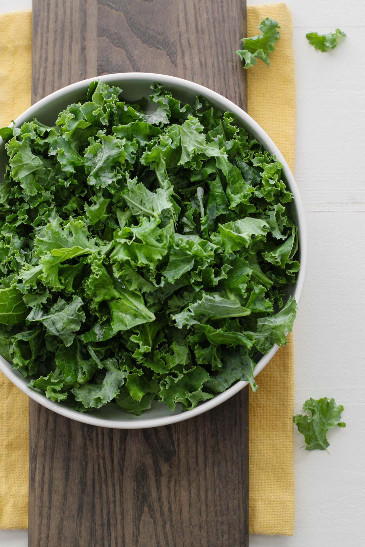 green kale in large salad bowl on wooden board with yellow towel underneath