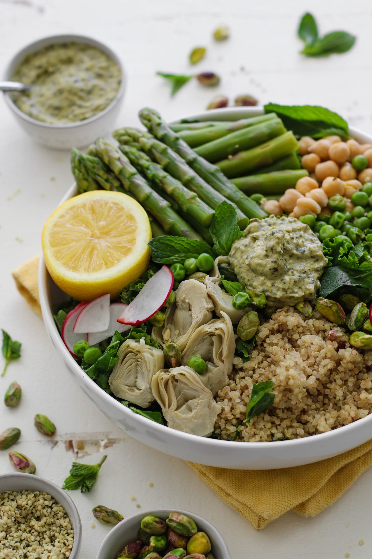 Spring Macro Bowl in large bowl with asparagus, lemon, artichoke hearts, sliced radishes, chickpeas, peas, quinoa, and mint
