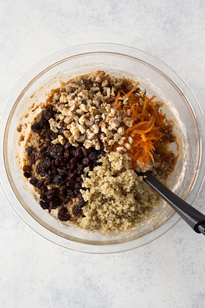 Quinoa Carrot Cake Breakfast Cookie dough in bowl with shredded carrots, walnuts, raisins, and quinoa mixed in with black spatula