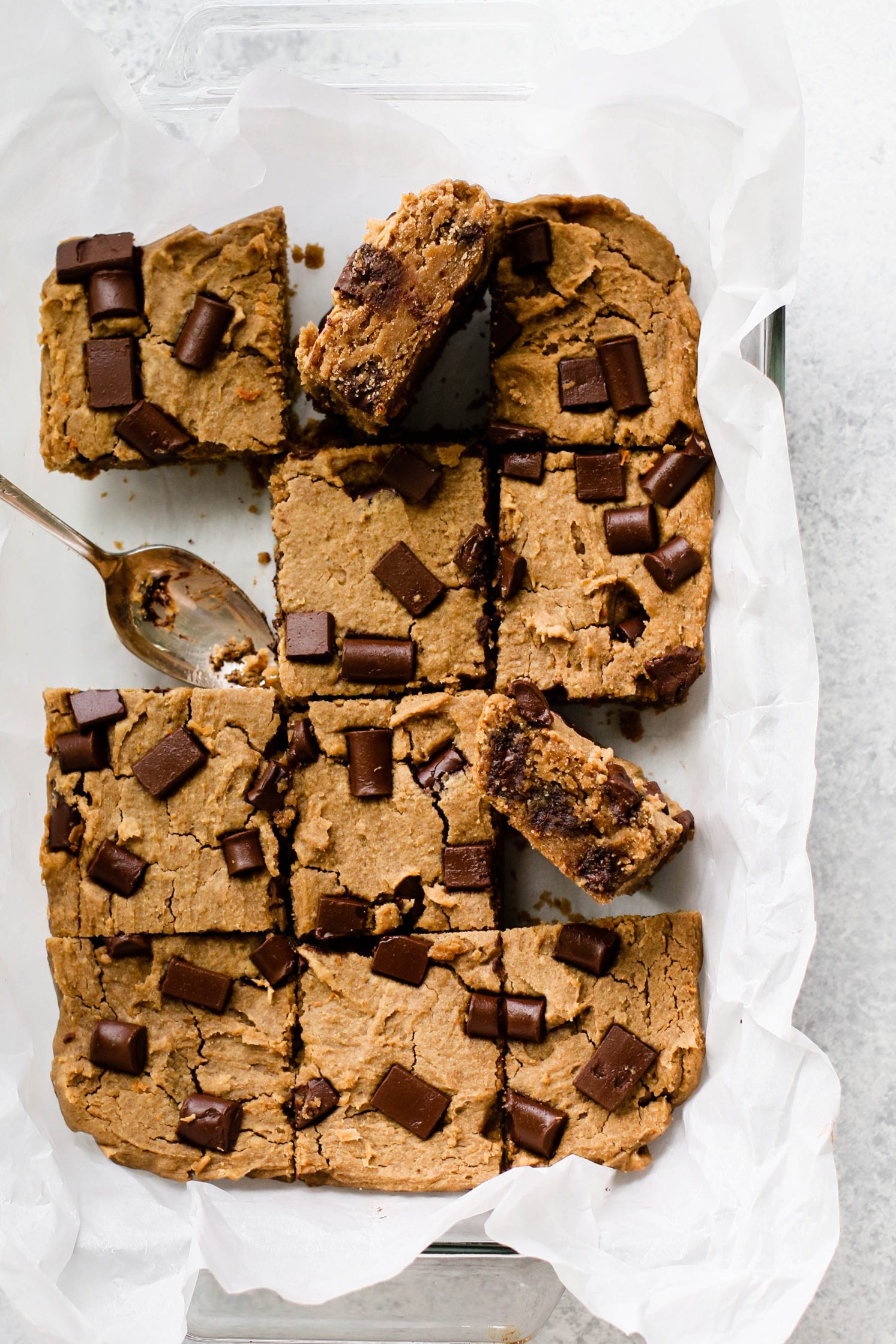 White Bean Blondies sliced in parchment lined baking dish with one missing and two pieces turned by Flora & Vino