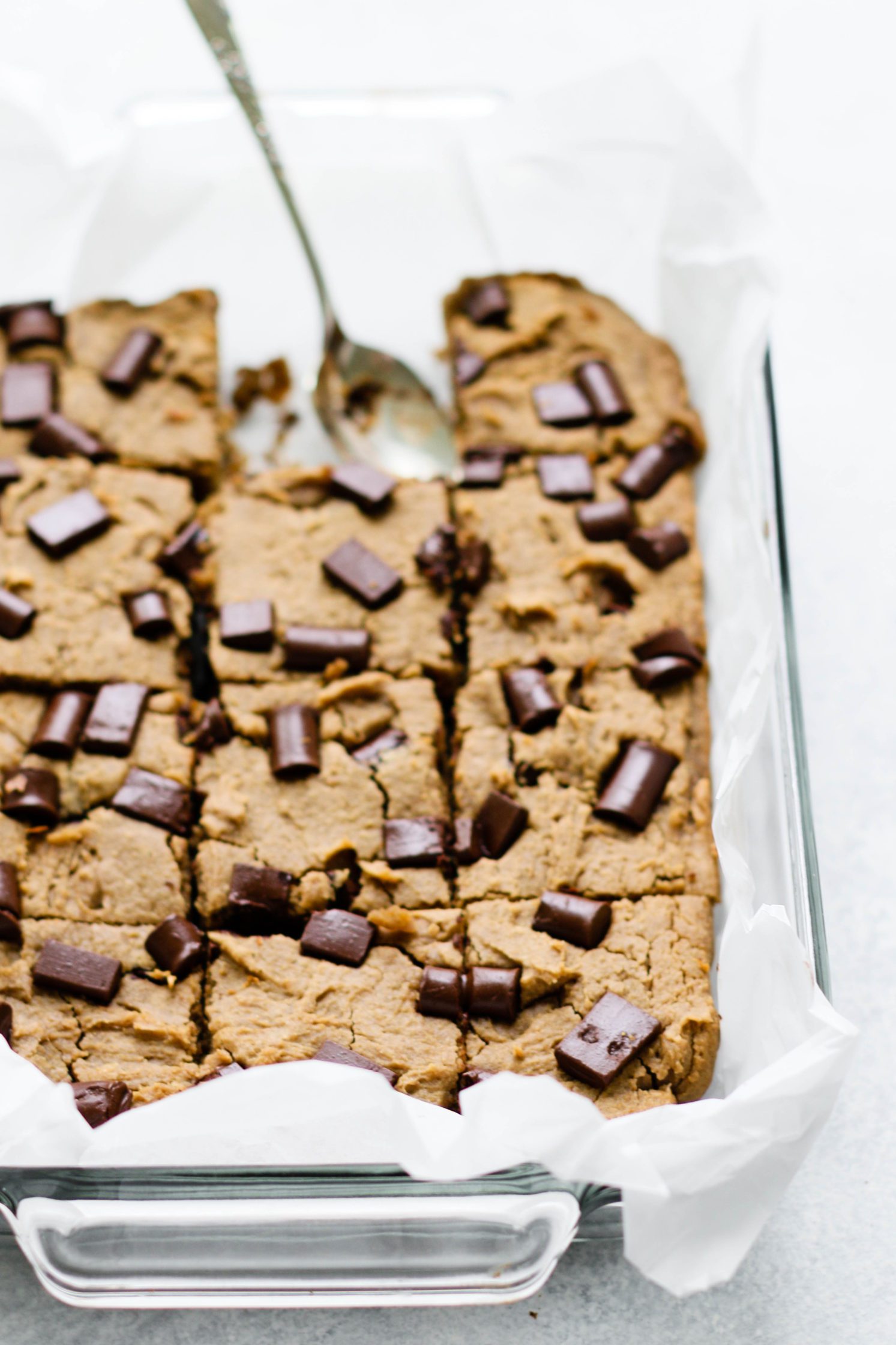 White Bean Blondies baked in parchment lined baking dish with one missing and a spoon
