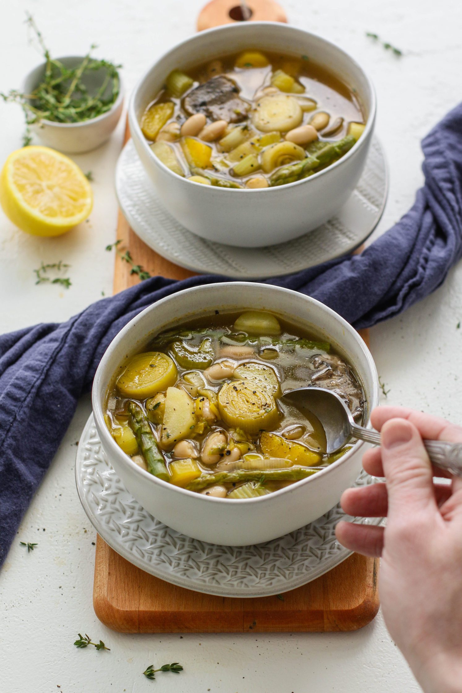 Spring Lemon-y Leek Soup served in bowls on a wooden board with two spoons and a bowl of thyme and half a lemon by Flora & Vino