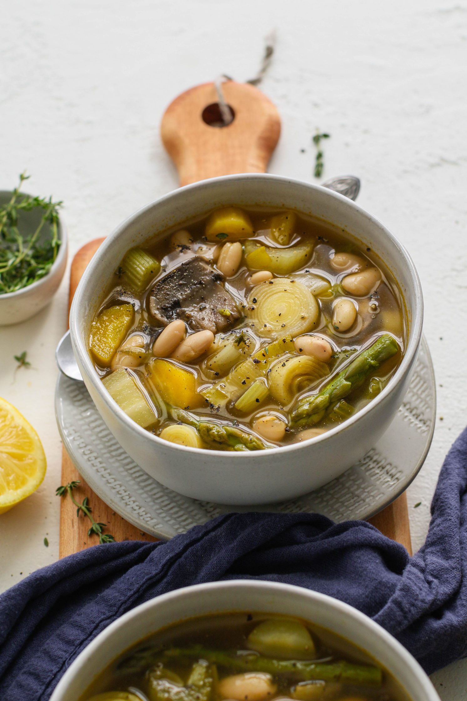 Spring Lemon-y Leek Soup served in bowls on a wooden board with two spoons and a bowl of thyme and half a lemon by Flora & Vino