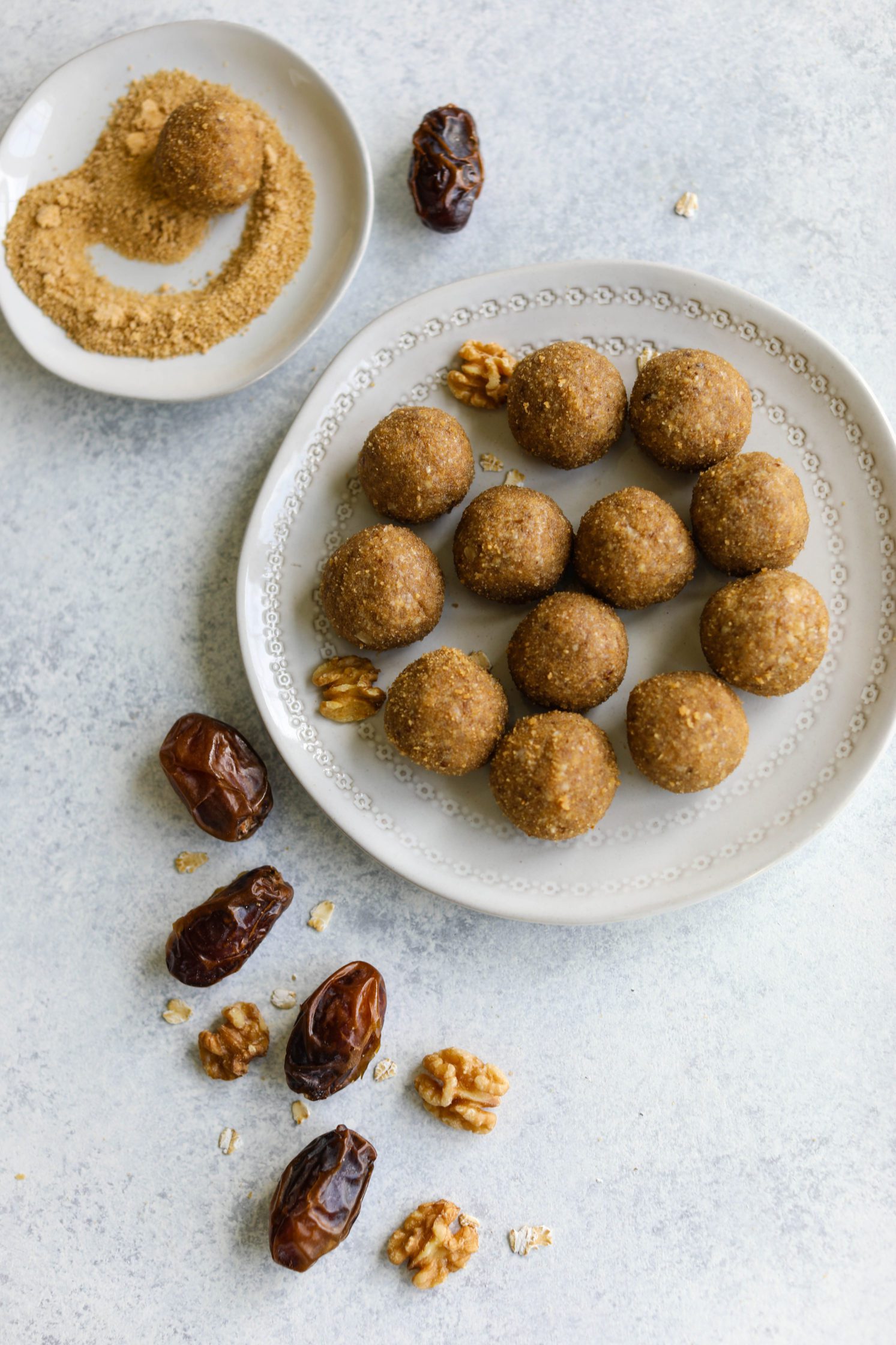 Maple Walnut Bliss Balls rolled in maple sugar on white plates with dates and walnuts scattered