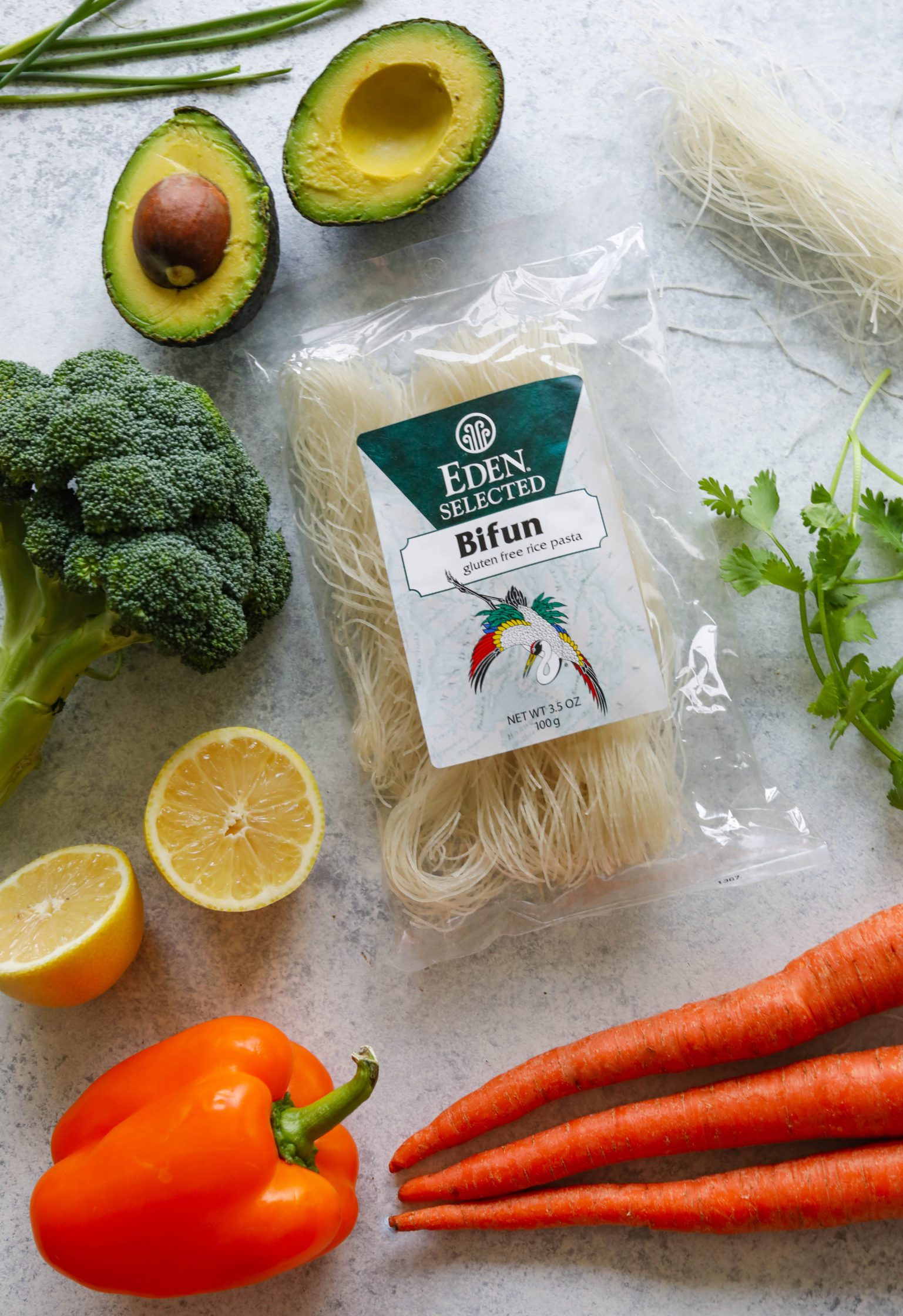 Eden Foods Bifun surrounded by broccoli, lemons, bell pepper, carrots, cilantro, rice noodles, and avocado 