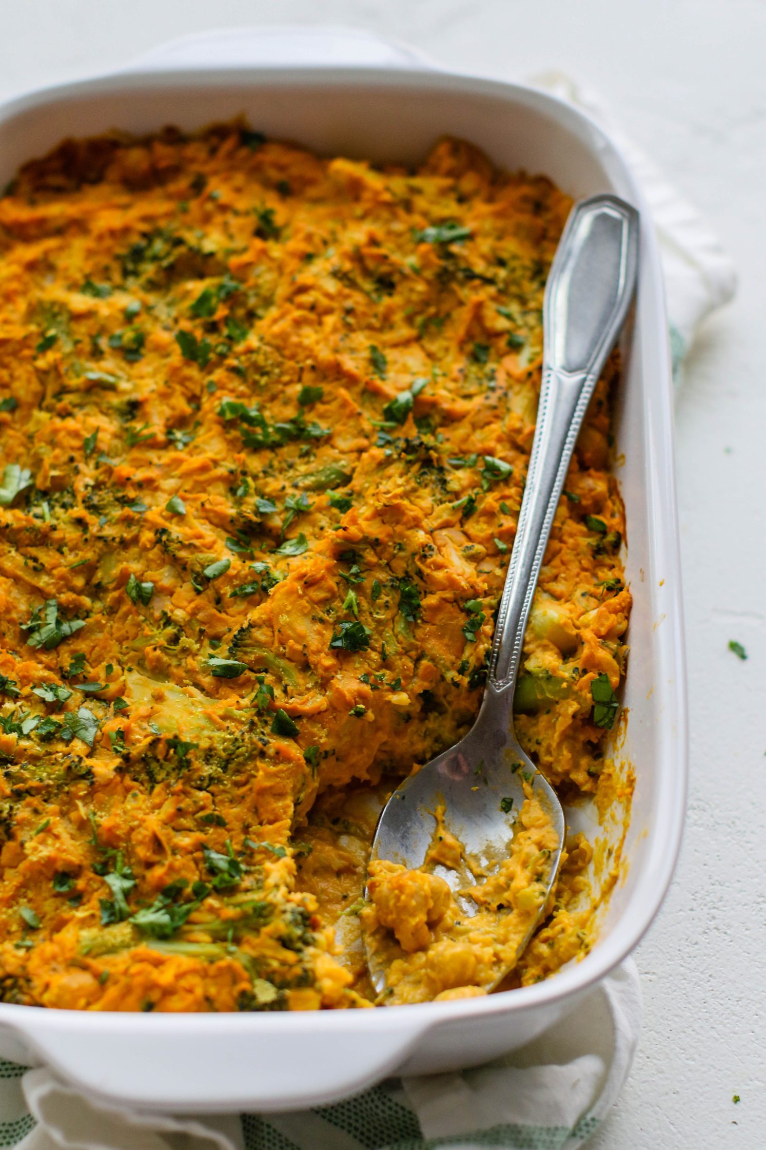 “Cheezy” Chickpea & Broccoli Casserole served in casserole dish with spoon by Flora & Vino