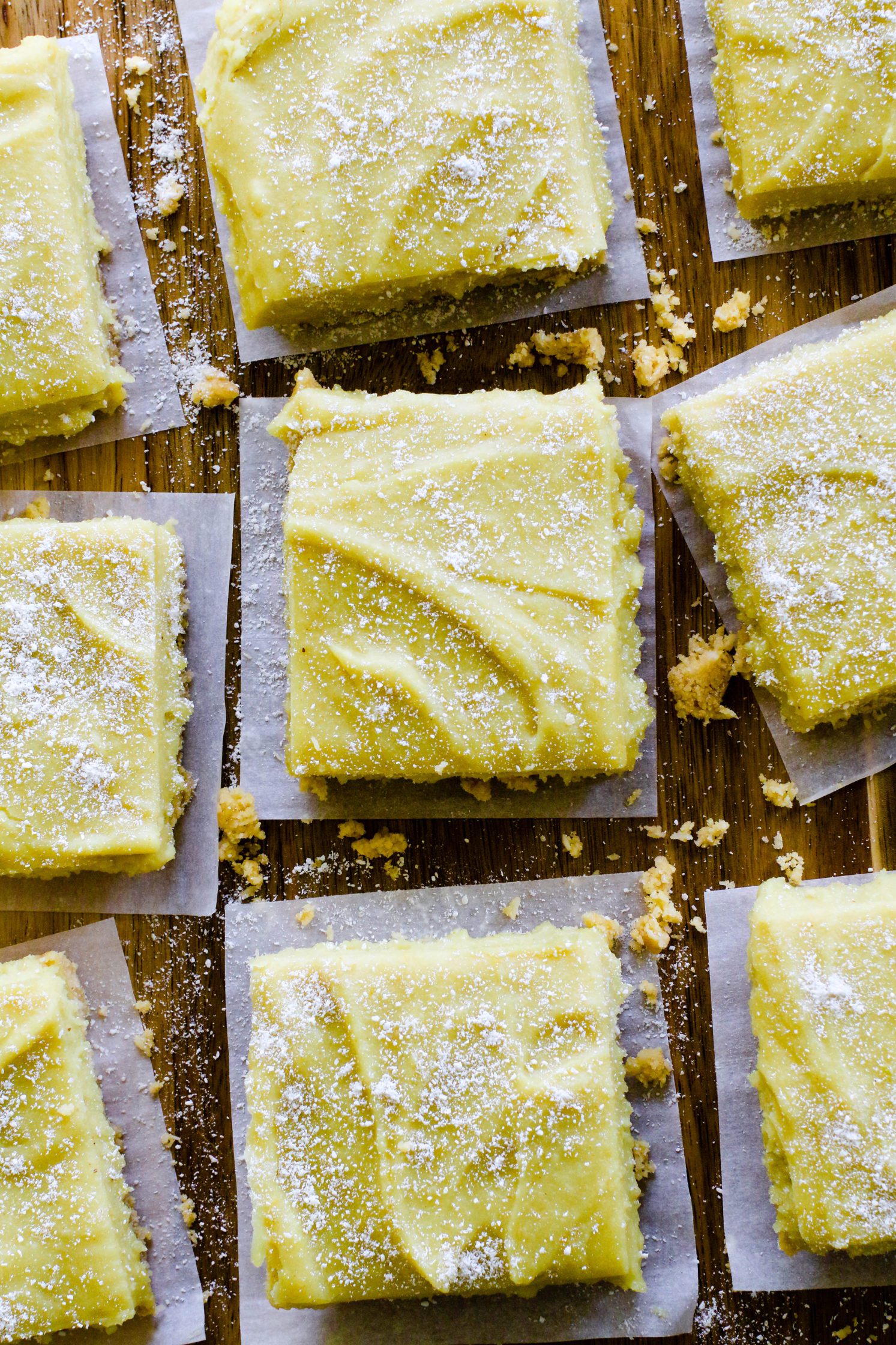 No-Bake Lemon Pie Bars spaced on wooden board with yellow background topped with coconut flour with lemons