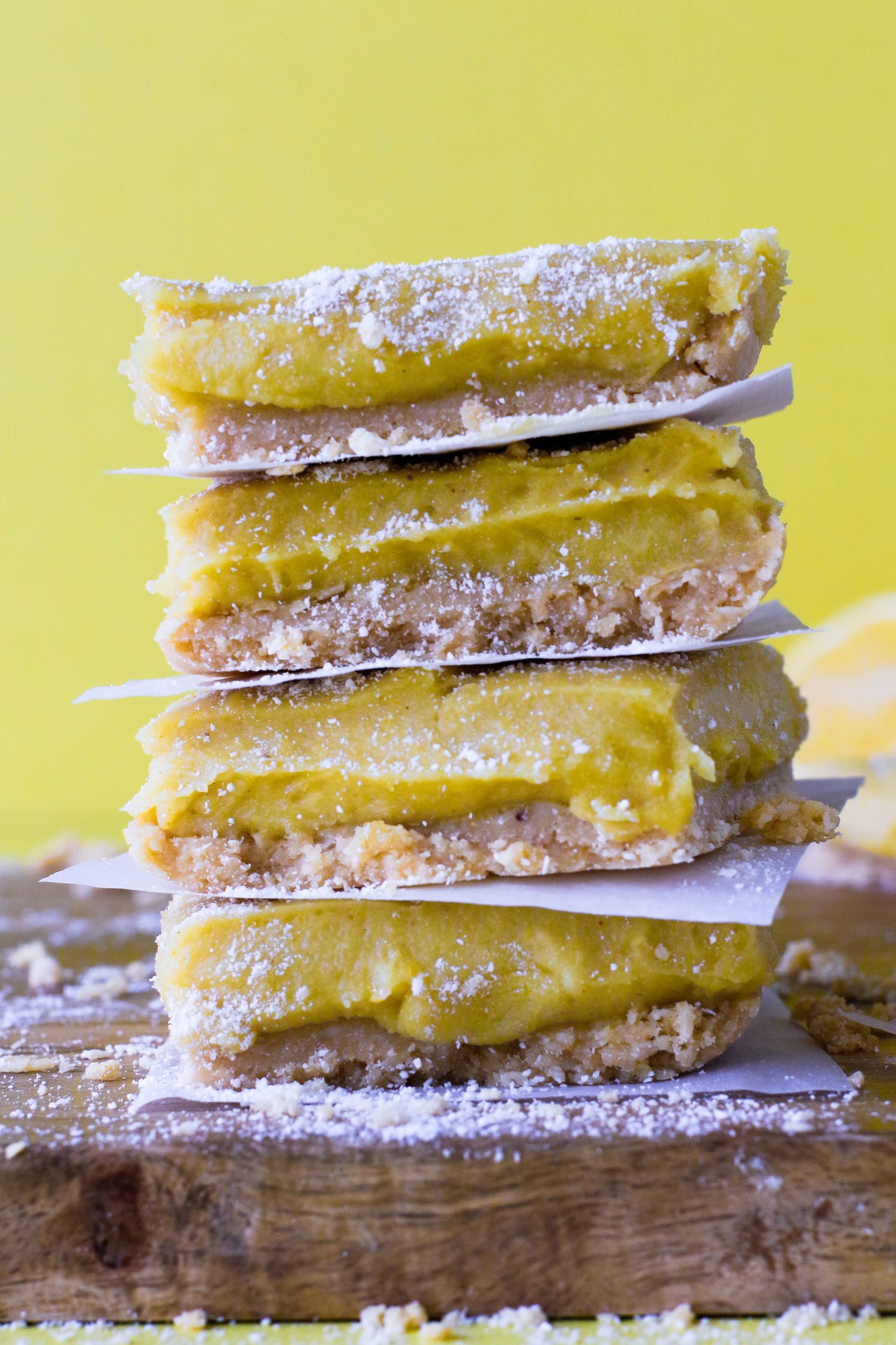 No-Bake Lemon Pie Bars stacked on wooden board with yellow background topped with coconut flour 