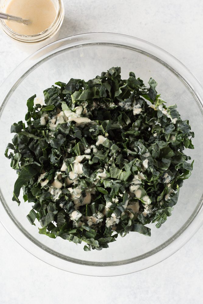 tahini dressing poured on chopped kale in mixing bowl