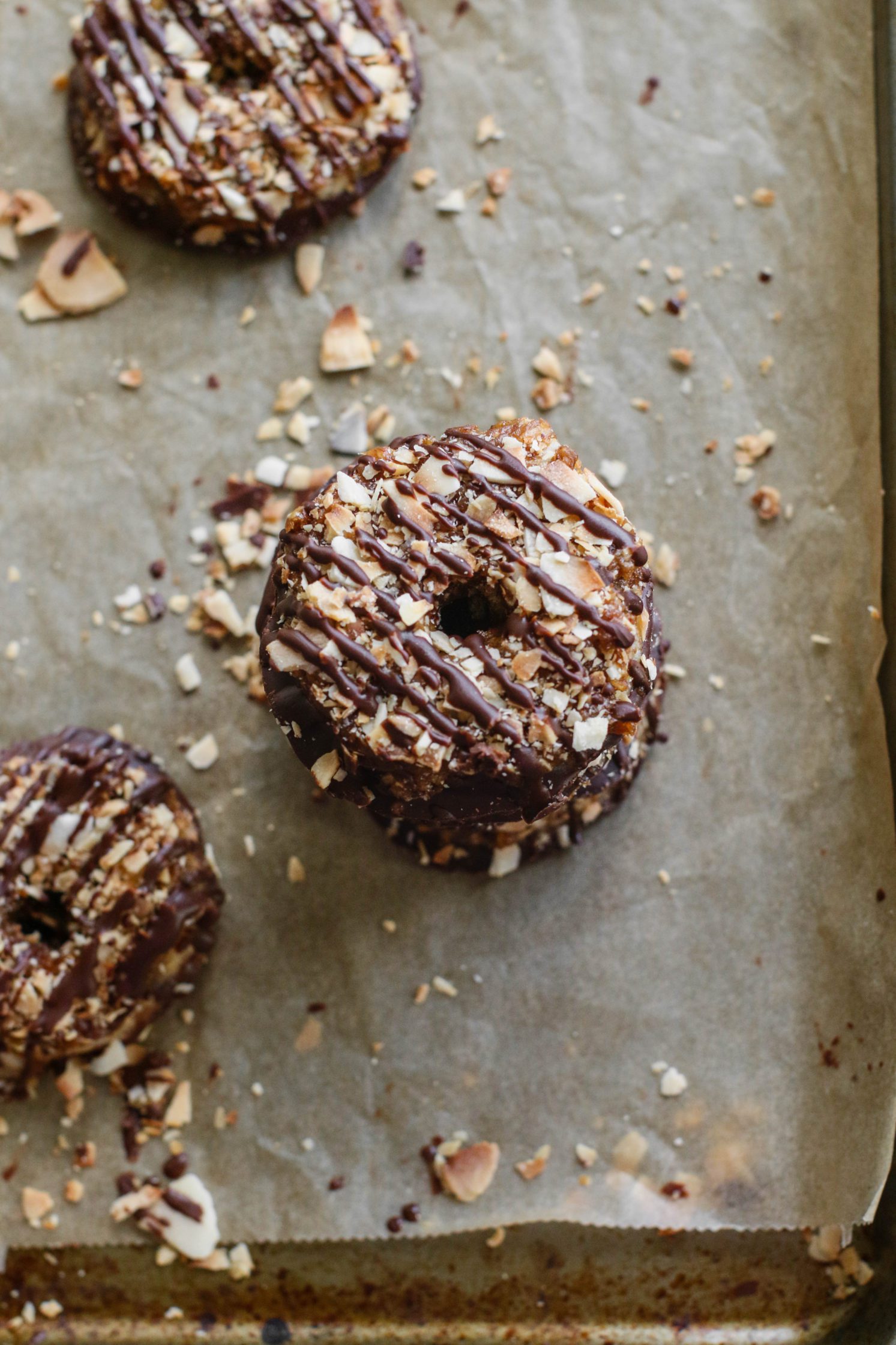 Vegan Toasted Coconut Samoas stacked on parchment lined baking sheet with scattered toasted coconut 