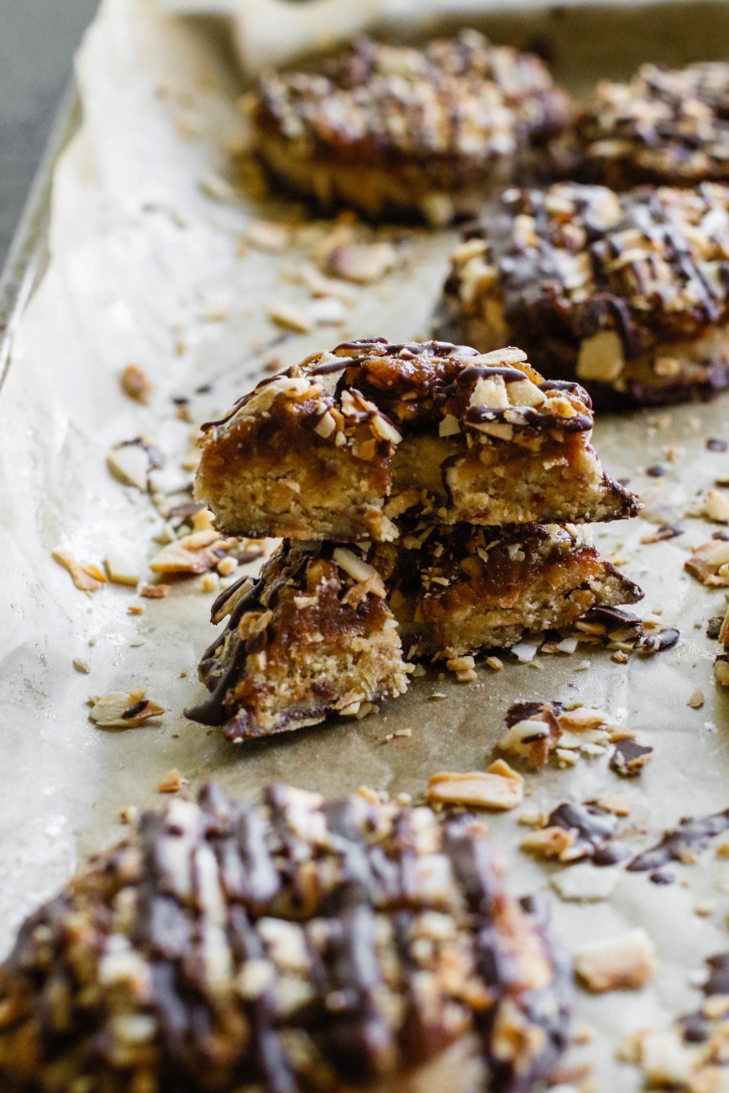 Vegan Toasted Coconut Samoas on parchment lined baking sheet with scattered toasted coconut and one cookie cut in half