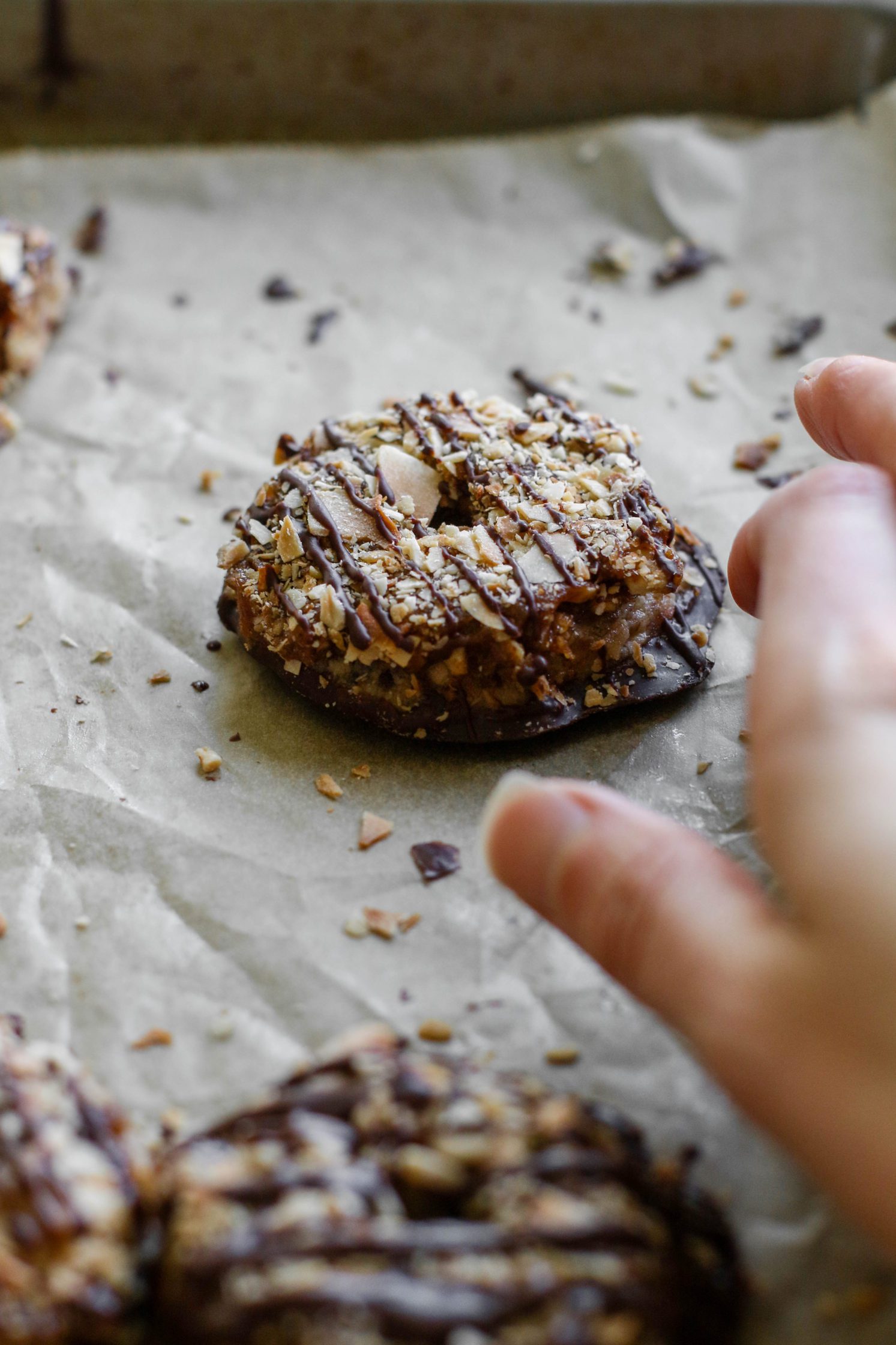 hand reaching for Vegan Toasted Coconut Samoas on parchment lined baking sheet with scattered toasted coconut 