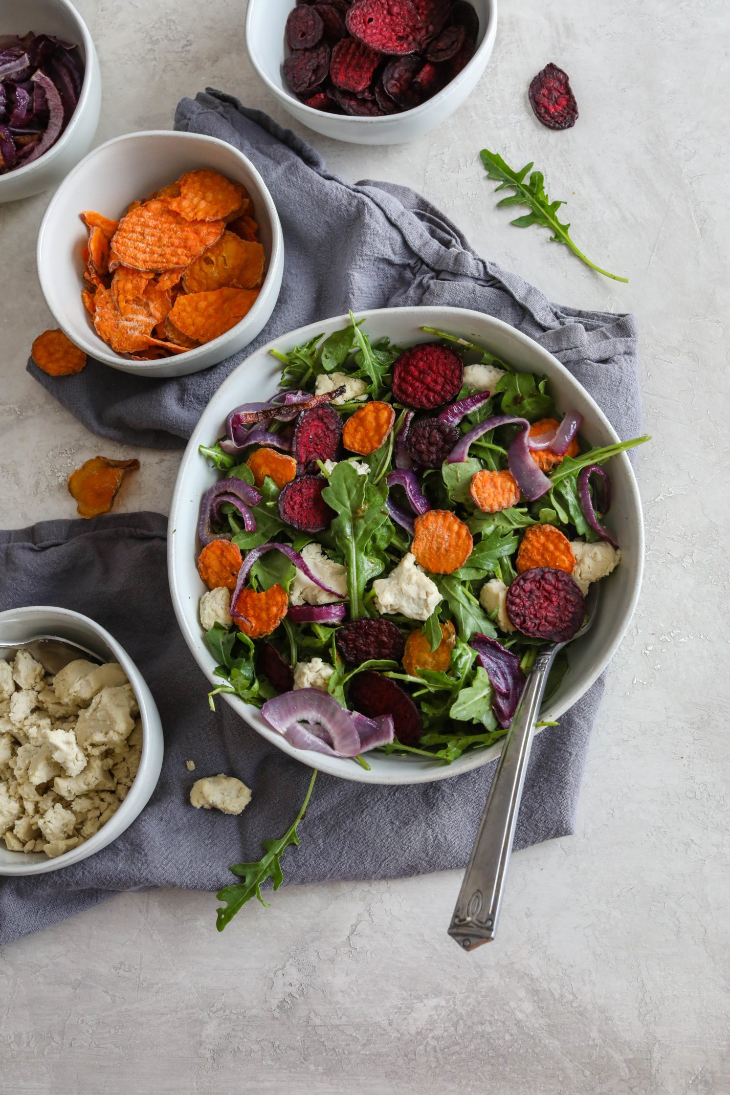 Root Veggie Chip Arugula Salad served on blue towel with scattered vegetable chips and fork