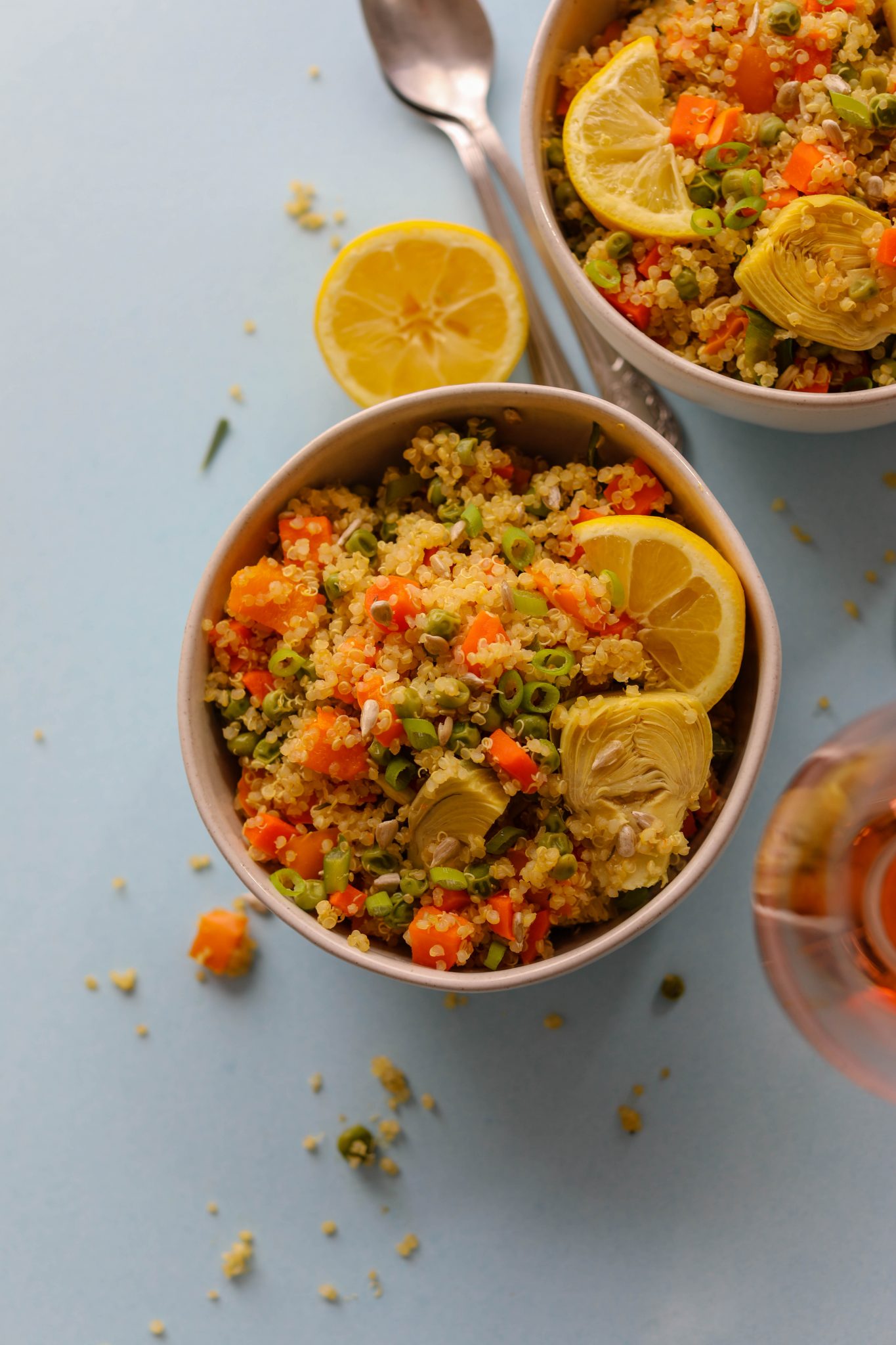Spring Quinoa Primavera served in bowls on blue paper with spoons and glass of Rosé