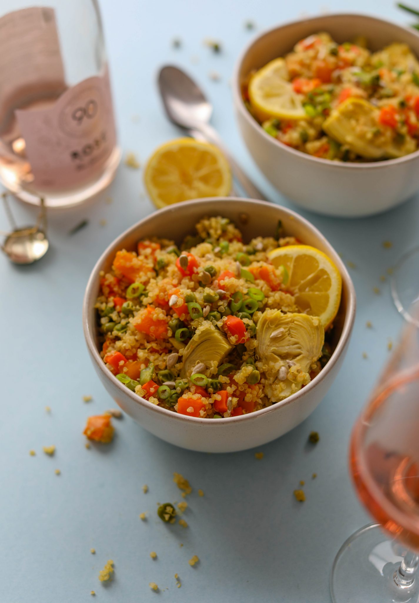 Spring Quinoa Primavera served in bowls on blue paper with spoons and glass of Rosé