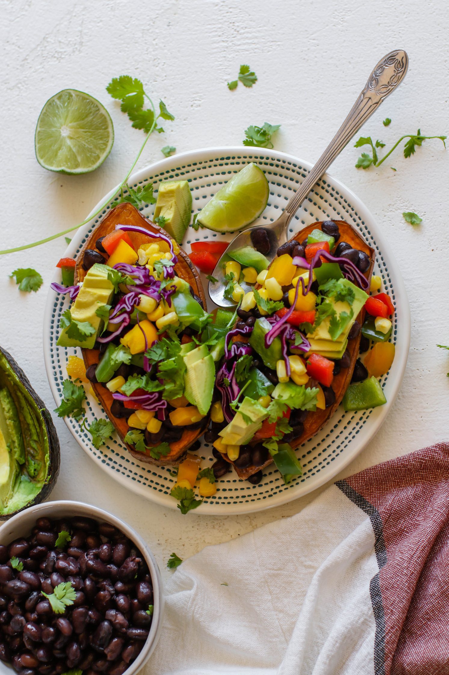 Copycat "Jammed Yam" served on plate with spoon, half of a lime, and shredded cilantro with black beans and avocado on the side