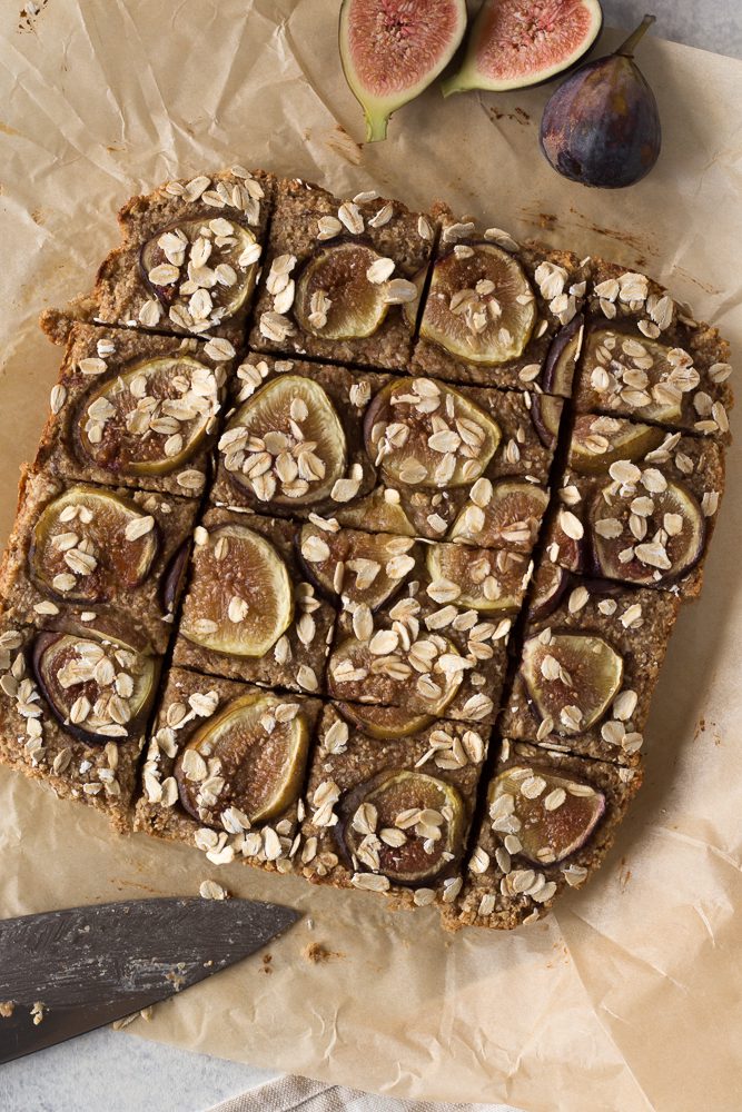 Fig Newton Breakfast Bars sliced on parchment paper with knife and fresh figs by Flora & Vino