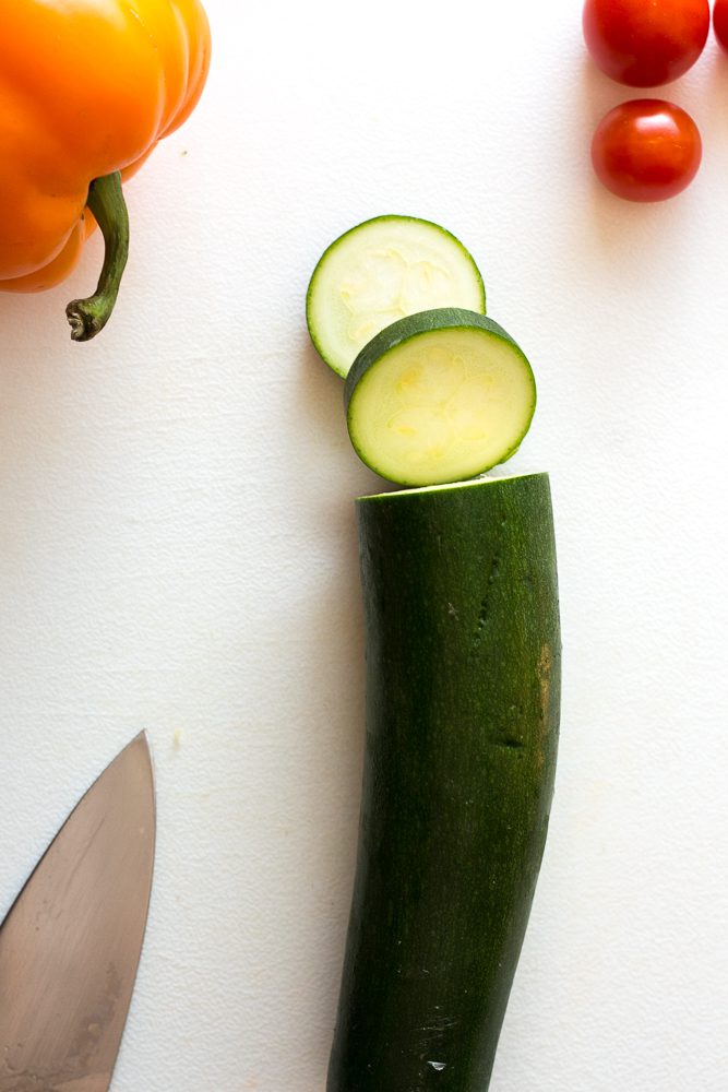 zucchini, bell pepper, and cherry tomato on cutting board with knife