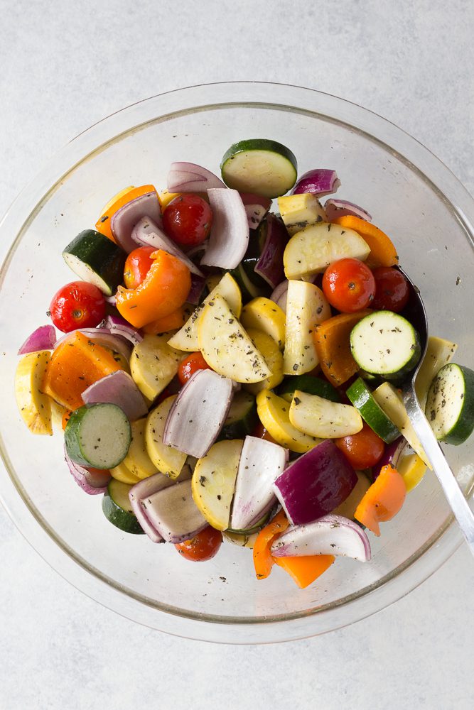 summer vegetables diced in glass bowl with spoon topped with seasonings