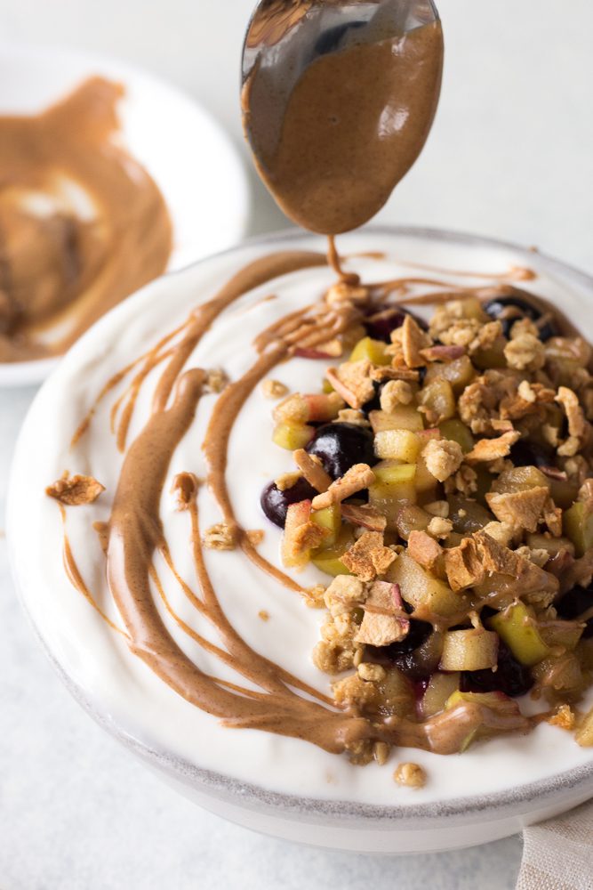 almond butter spoon drizzling on Apple Pie Yogurt Bowl by Flora & Vino