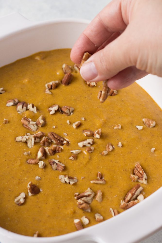 hand sprinkling pecans on pumpkin apple bake