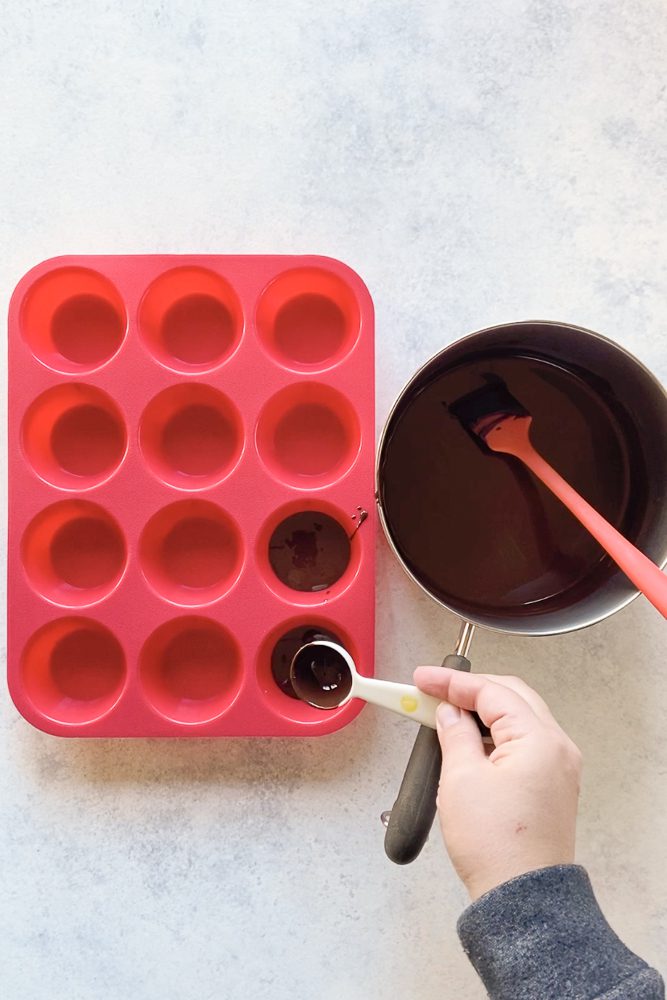 hang pouring melted chocolate in a silicone muffin tin by Flora & Vino
