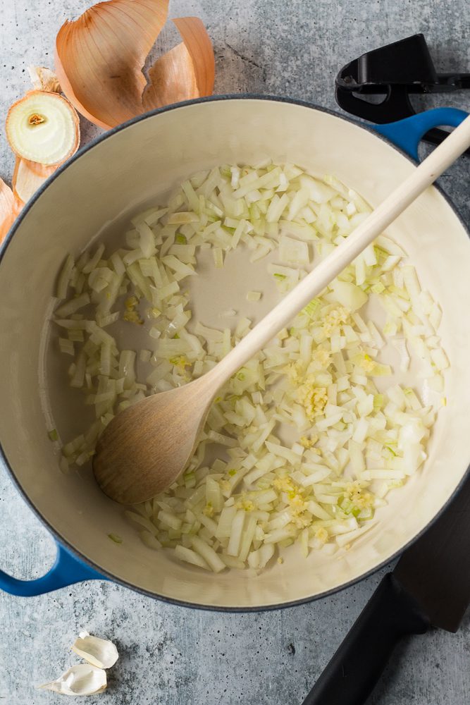 white onions sautéed in a pot with a wooden spoon by Flora & Vino