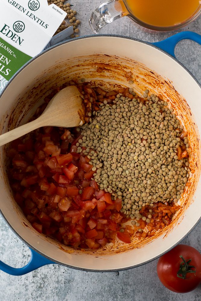 Lentil Tomato Soup in a pot with a wooden spoon by Flora & Vino 