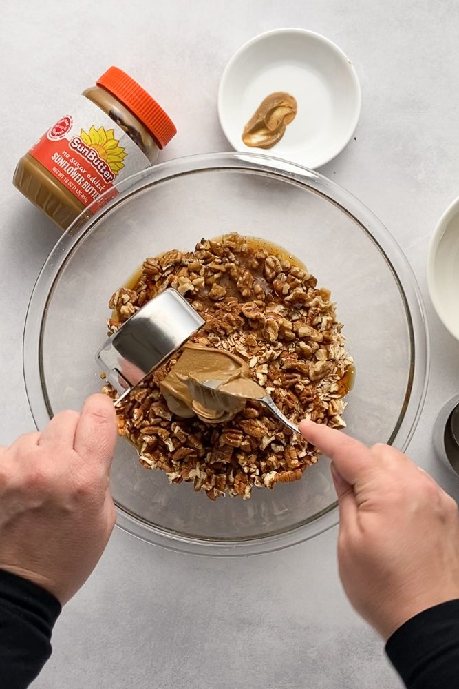 hands mixing granola together in glass bowl with SunButter jar on the side