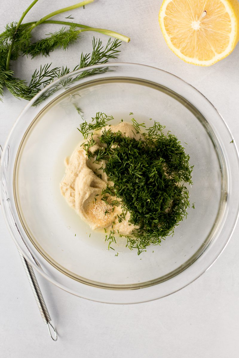 hummus and dill in mixing bowl with half lemon and dill on the side
