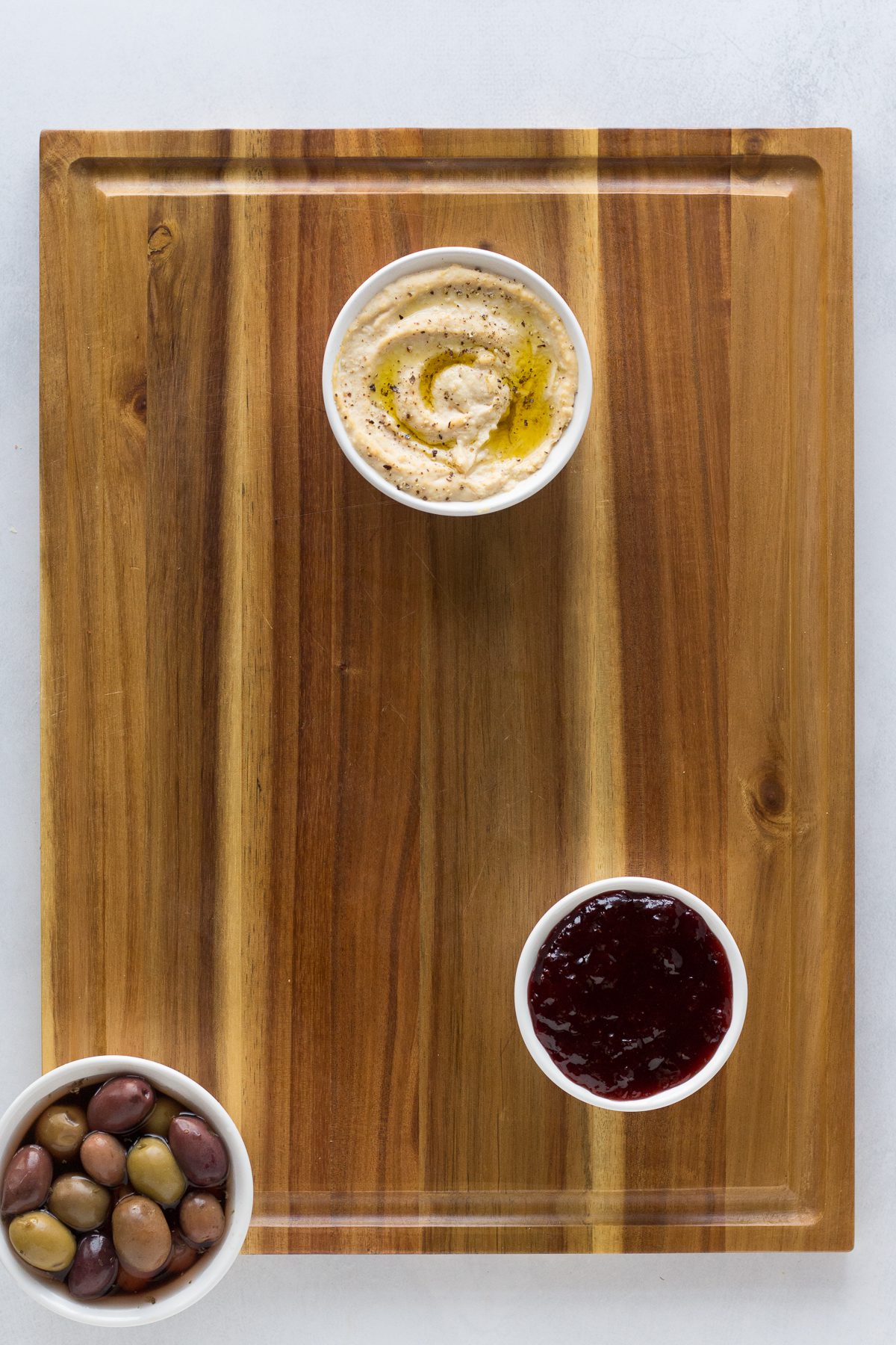 vegan board with hummus, olives, and jam on wooden board by Flora & Vino