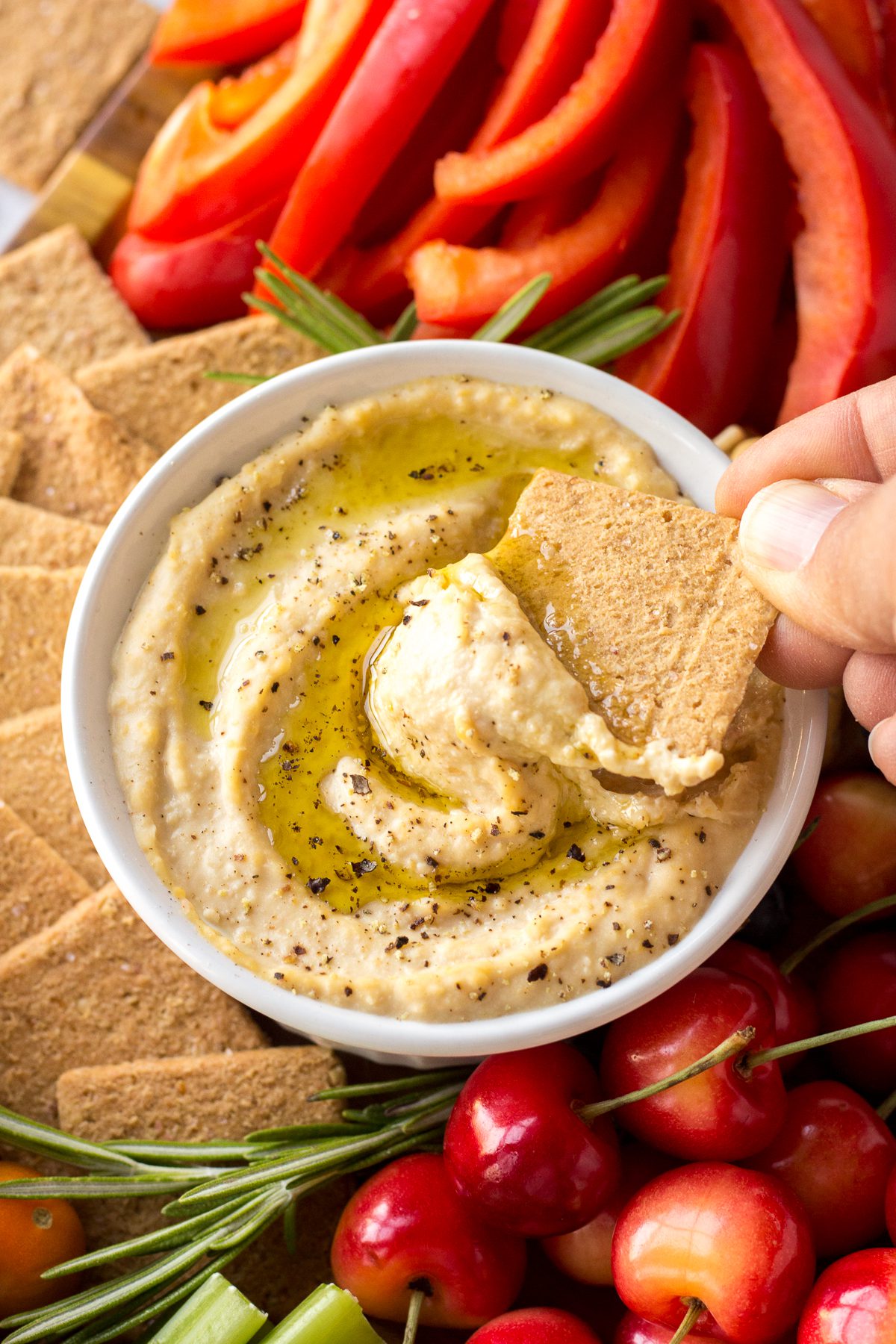 hand dipping cracker into hummus from Vegan Cheese Board by Flora & Vino