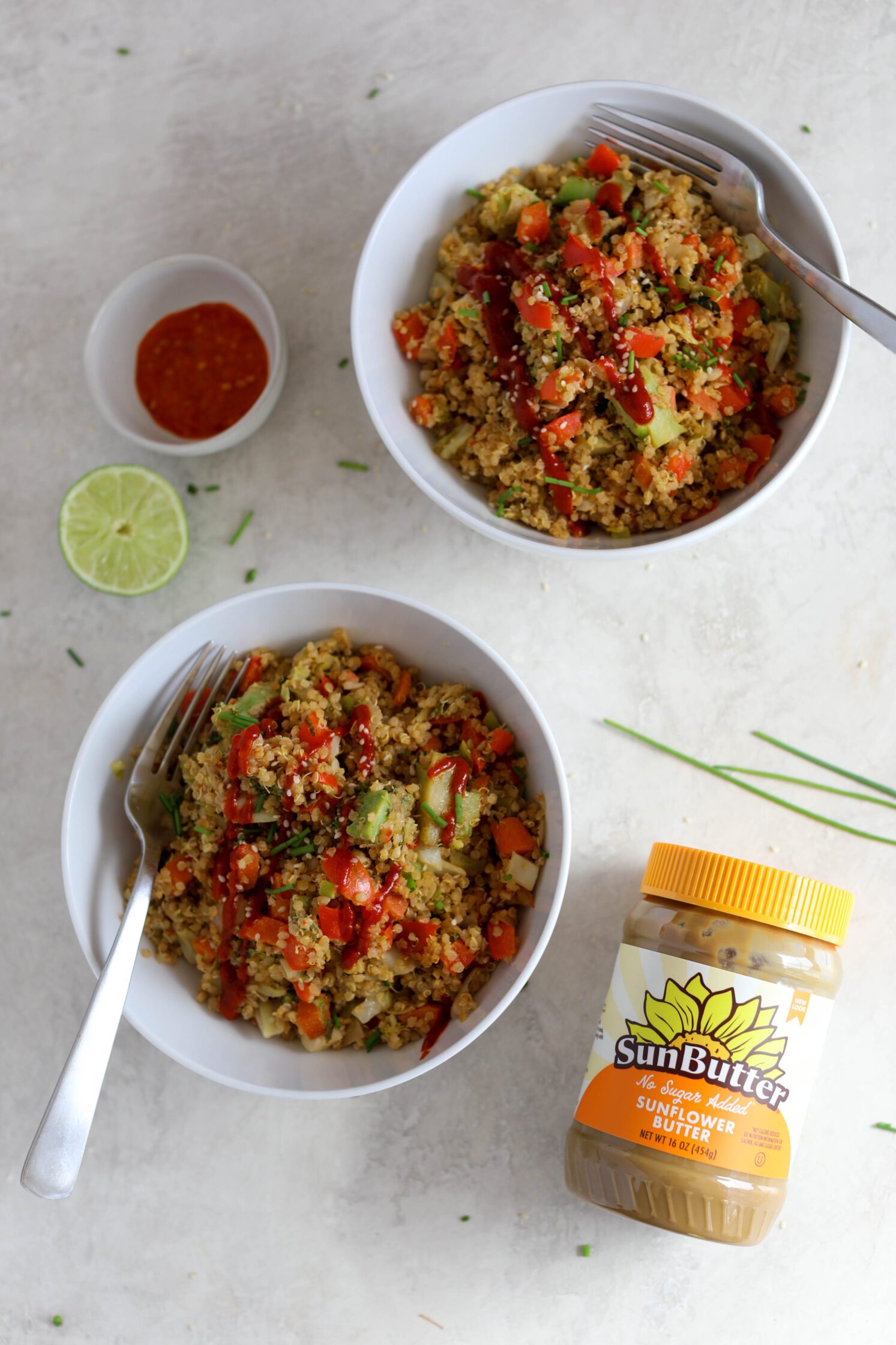 SunButter Quinoa Fried Rice served in bowls with forks and sriracha, sesame seeds, and chives by Flora & Vino