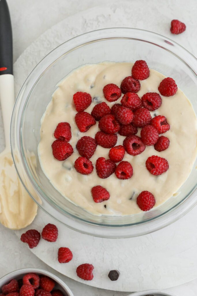 white bean blondie batter with raspberries on top and spatula on the side by Flora & Vino