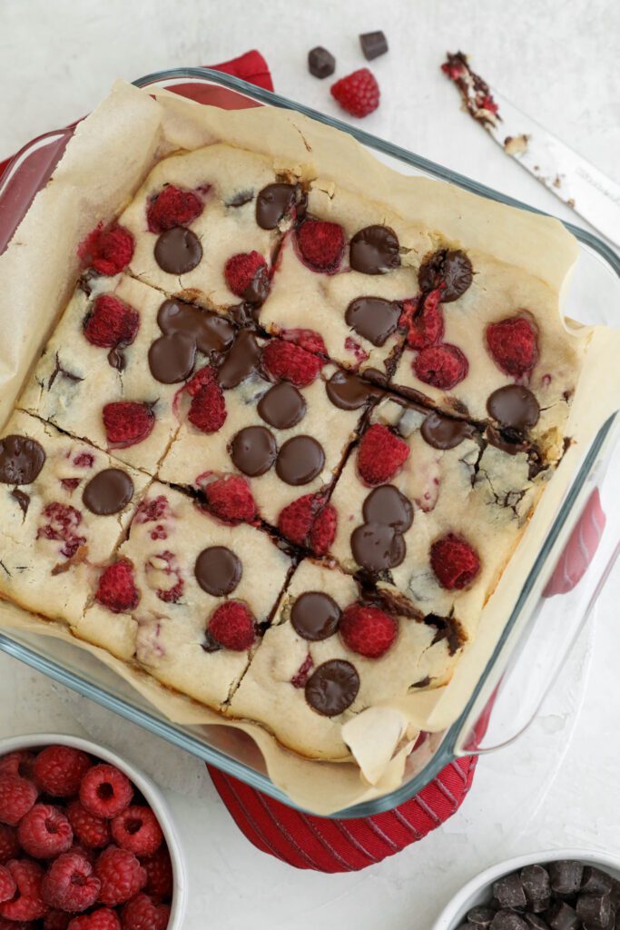 Dark Chocolate Raspberry Blondies baked and cut into nine squares in parchment lined baking dish by Flora & Vino