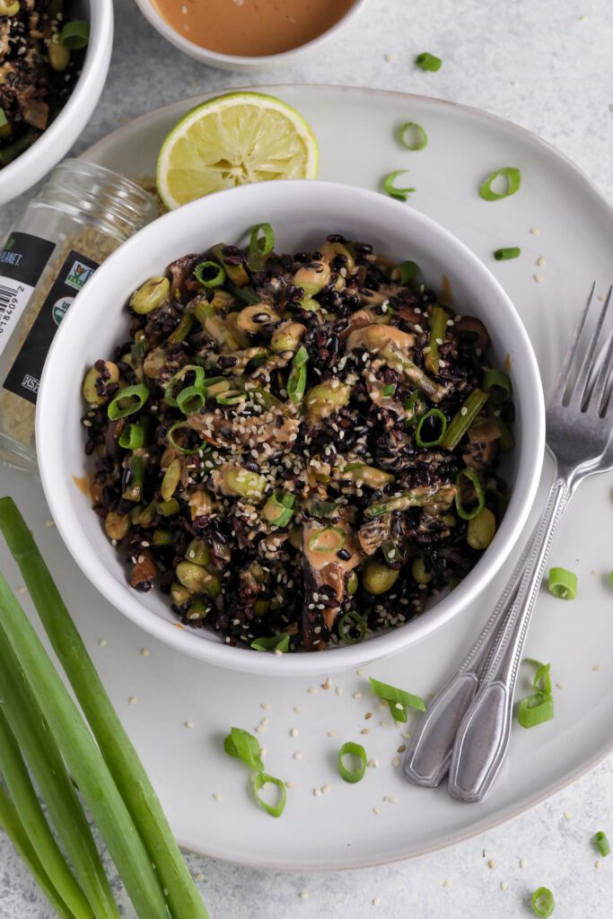 Forbidden Fried Rice served in white bowl topped with green onion and white sesame seeds with lime and spicy sriracha aioli on the side with two forks