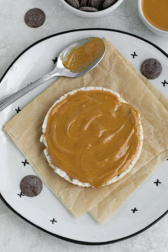rice cake on parchment lined plate topped with peanut butter with scattered cacao wafers