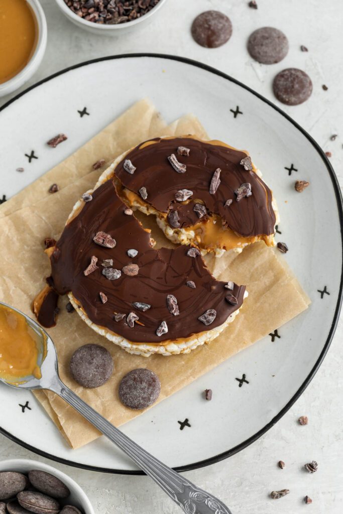 Chocolate Peanut Butter Rice Cake served on parchment paper lined plate with scattered cacao nibs, chocolate wafers, and peanut butter
