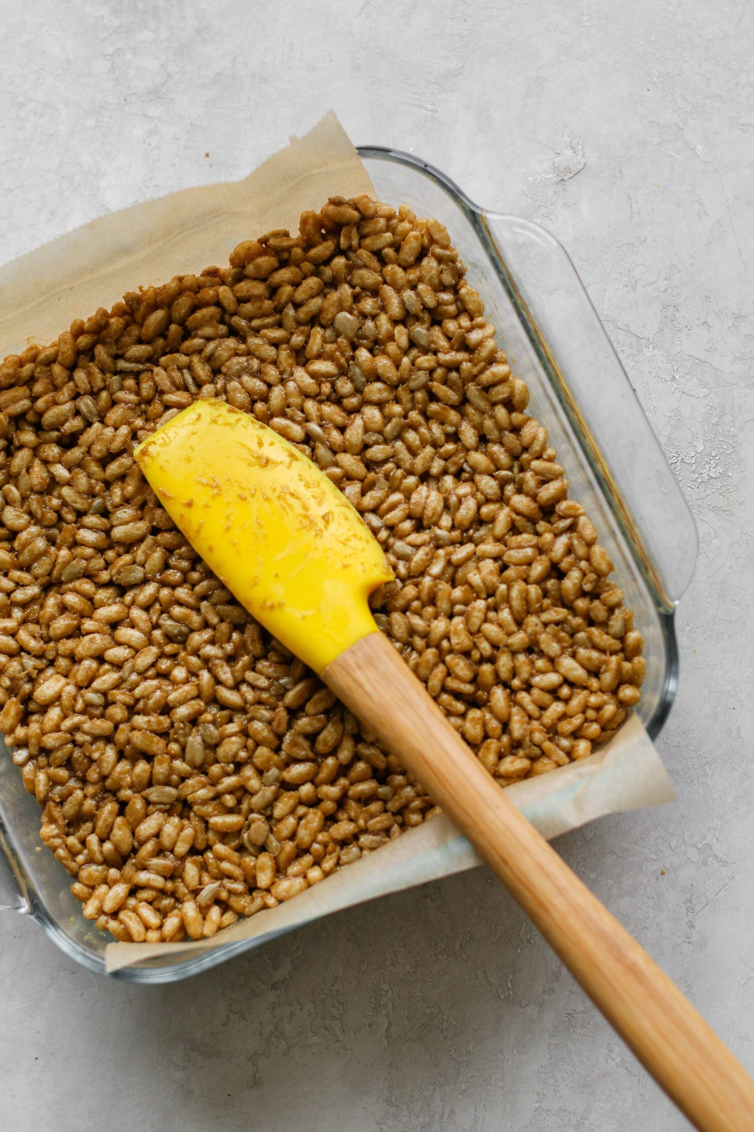 Rice Crispy Treats pressed into parchment lined baking dish with spatula 