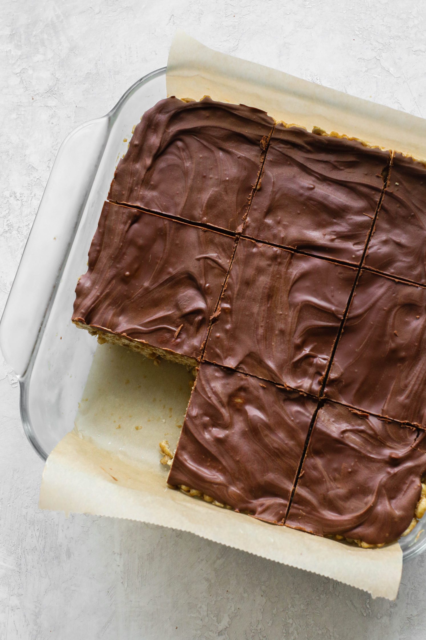 Chocolate SunButter Rice Crispy Treats sliced into bars in parchment lined baking dish